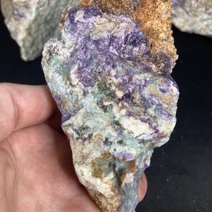 May include: A rough, irregularly shaped piece of purple and green amethyst with a brown, rocky exterior.