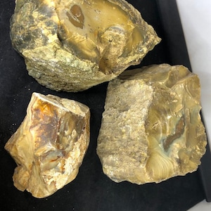 Puede incluir: Tres piezas de ágata de forma irregular, cada una con un patrón y un color diferentes. La ágata es de color marrón claro, beige y blanco con una calidad translúcida. La ágata es una piedra natural.