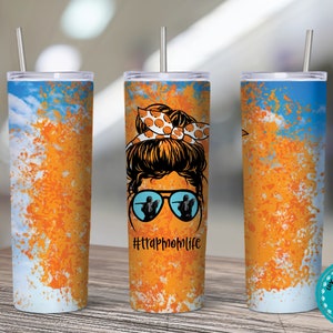 Op de afbeelding: Een roestvrijstalen tumbler met een blauw en oranje splatter-paintontwerp. De tumbler heeft een afbeelding van een vrouw met een stippen strik en zonnebril. De tekst "#trapmomlife" is op de tumbler gedrukt.