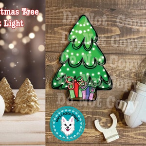 May include: A Christmas tree night light with a green tree design, featuring white lights and wrapped gifts. The night light has a white base and a clear bulb. The image also includes a snowman and two gold glitter trees.