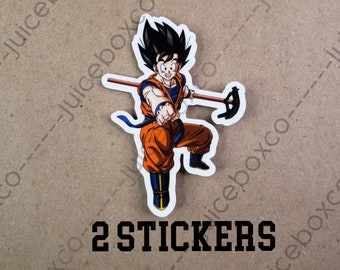 May include: Two stickers featuring a cartoon character with black hair, an orange gi, and a blue sash. The character is holding a staff and has a determined expression. The text "2 STICKERS" is printed below the image.