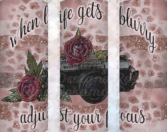May include: A pink and gold tumbler with a leopard print design and a vintage camera graphic. The tumbler has the text "when life gets blurry adjust your focus" on it.