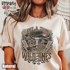 May include: A beige t-shirt with a graphic print of a skull with horns and the text "I got a thing for the wild ones".