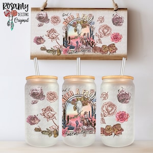 May include: Three clear glass tumblers with a white background and a design of a cowboy riding a horse with a skull and crossbones in the background. The design is surrounded by pink roses. The tumblers have a bamboo lid and a metal straw.