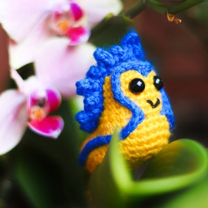 May include: A crocheted seahorse toy made with blue and yellow yarn. The toy is resting on a green leaf.