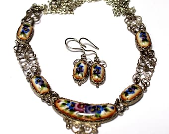 Peut inclure: Un collier et des boucles d'oreilles en argent avec des pendentifs en porcelaine florale. Le collier a une chaîne délicate avec un pendentif plus grand au centre. Les boucles d'oreilles sont de forme ovale avec des motifs floraux.