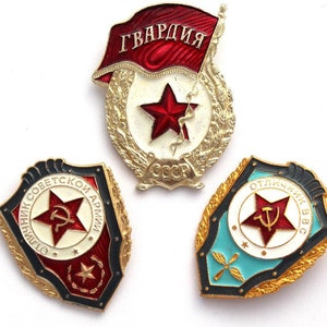 Puede incluir: Tres insignias militares soviéticas vintage. La insignia superior es roja y dorada con la palabra "ГВАРДИЯ" (Guardia) en escritura cirílica. La insignia de la izquierda es roja, dorada y negra con el texto "ВОИННИК СОВЕТСКОЙ АРМИИ" (Soldado del ejército soviético) en escritura cirílica. La insignia de la derecha es azul, dorada y roja con el texto "ОТЛИЧНИК ВВС" (Excelente de la Fuerza Aérea) en escritura cirílica.
