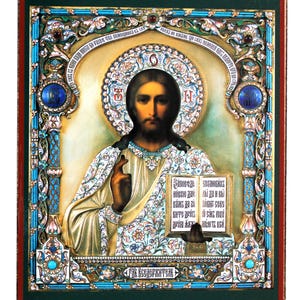 May include: A rectangular religious icon featuring a central figure of Christ with long dark hair, holding an open book with Cyrillic text and making a blessing gesture. The frame is ornate with blue, gold, and floral enamel detailing.