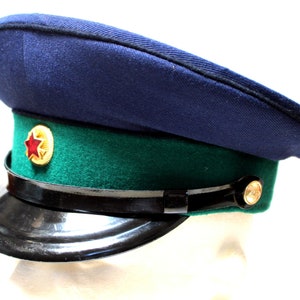 Op de afbeelding: Een donkerblauwe militaire hoed met een groene band en een rood sterembleem. De hoed heeft een zwarte leren rand.