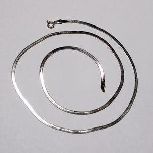 May include: A silver snake chain necklace. The chain is made of small, flat links that are woven together in a herringbone pattern.