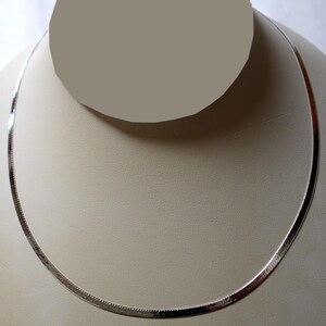 May include: A silver chain necklace with a herringbone pattern. The necklace is displayed on a white mannequin bust.