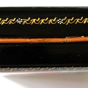 May include: A black lacquered wooden box with a gold painted design. The box has a hinged lid and a copper colored metal hinge.