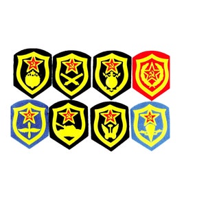 Puede incluir: Ocho parches bordados en forma de escudos con una estrella roja y detalles amarillos. Los parches presentan diferentes símbolos militares, incluyendo un tanque, un avión y un arma.