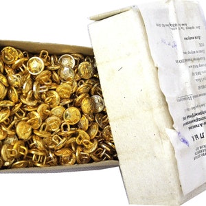 Może przedstawiać: Pudełko wypełnione złotymi guzikami. Każdy guzik ma pięcioramienną gwiazdę i pętelkę z tyłu. Pudełko jest oznaczone tekstem w języku cyrylicy.