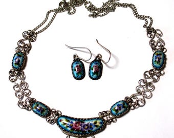 Peut inclure: Un collier et des boucles d'oreilles en argent avec émail bleu et motifs floraux peints à la main. Le collier présente un pendentif en forme de croissant de lune avec un motif floral plus grand.