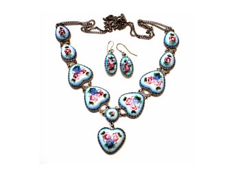 Peut inclure: Un collier et des boucles d'oreilles en argent avec des cœurs en émail bleu décorés de fleurs roses et bleues peintes à la main.