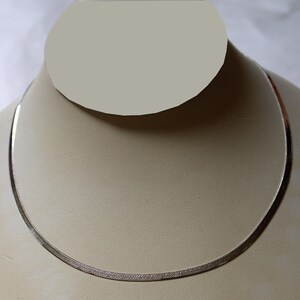 May include: A silver chain necklace on a white display stand. The chain is a herringbone style.