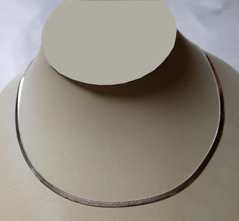 May include: A silver chain necklace on a white display stand. The chain is a herringbone style.