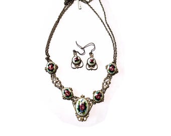 Peut inclure: Un ensemble de bijoux vintage comprenant un collier et des boucles d'oreilles assorties. Le collier et les boucles d'oreilles ont un sertissage en métal argenté avec des motifs floraux. Le collier a un pendentif central ovale et des pendentifs ronds plus petits.
