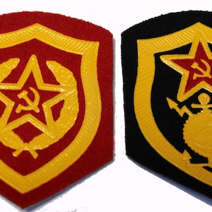 Puede incluir: Dos parches bordados con una estrella roja y un emblema de martillo y hoz. El parche de la izquierda está sobre un fondo rojo con un borde amarillo y una corona. El parche de la derecha está sobre un fondo negro con un borde amarillo y un ancla y una brújula.