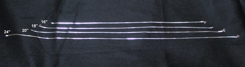 May include: Four silver chains of different lengths, 16 inches, 18 inches, 20 inches, and 24 inches, laid out on a black surface.