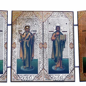 May include: A five-panel folding icon screen featuring religious figures in traditional robes against intricate silver and gold patterned backgrounds. Each vertical panel depicts a standing saint with a halo, rendered in muted tones of red, green, and gold.