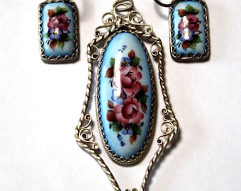 Peut inclure: Un ensemble de pendentif et boucles d'oreilles en argent avec émail bleu et motifs floraux peints à la main. Le pendentif présente une grande pièce ovale avec un design filigrané délicat.