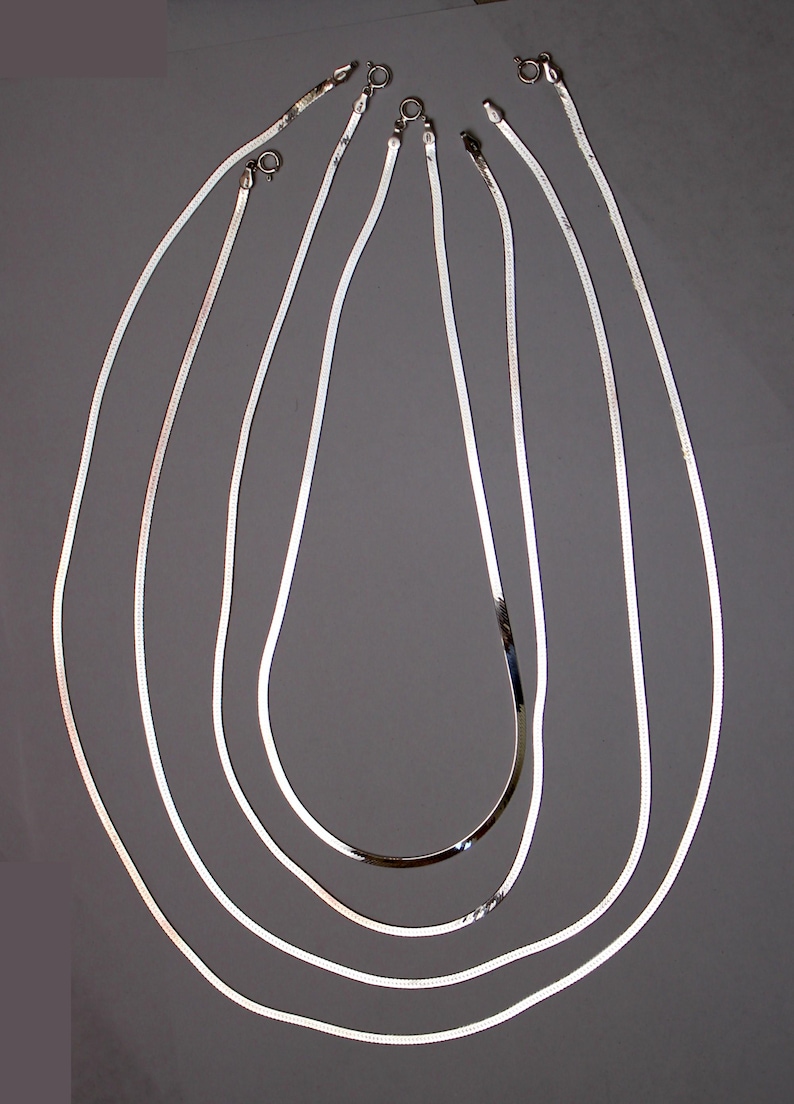 May include: Five silver snake chains of varying lengths, displayed on a gray background.