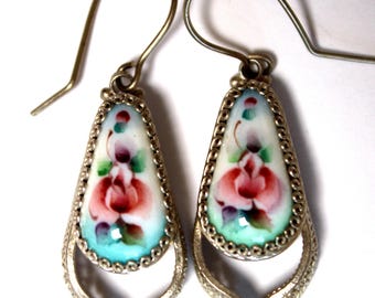 Peut inclure: Une paire de boucles d'oreilles pendantes en argent avec un pendentif en porcelaine en forme de larme orné d'un motif floral peint à la main dans des tons de rose, vert et bleu.