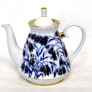 Könnte beinhalten: Eine weiße Porzellan-Teekanne mit einem blauen und goldenen Blumendesign. Die Teekanne hat einen Deckel und einen Griff. Das Blumendesign zeigt blaue Glocken und goldene Akzente.