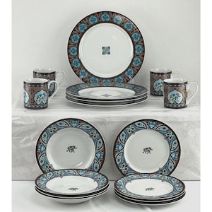 Puede incluir: Un juego de vajilla completo con platos, cuencos y tazas. Las piezas de cerámica blanca tienen un borde decorativo marrón y azul con un diseño intrincado. Algunos platos y cuencos tienen un motivo de elefante en el centro.