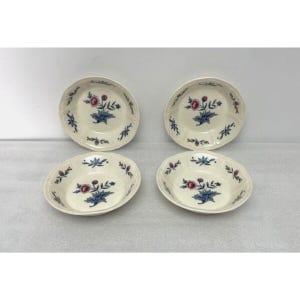 May include: Four off-white ceramic bowls with a floral design. Each bowl features a central cluster of blue leaves and red flowers, surrounded by smaller floral accents. The bowls have a scalloped edge.