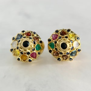 May include: A pair of gold earrings with a circular design featuring a variety of colorful gemstones, including red, green, blue, yellow, and white.