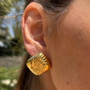 May include: Gold-toned square-shaped earrings with a textured, swirling design.