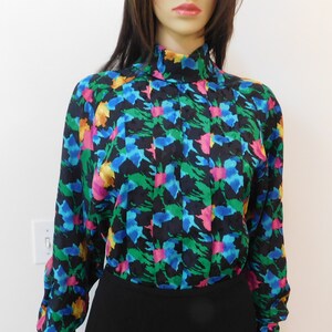 May include: A black, long-sleeved blouse with a high neck and a colorful abstract print featuring shades of blue, green, pink, and yellow.