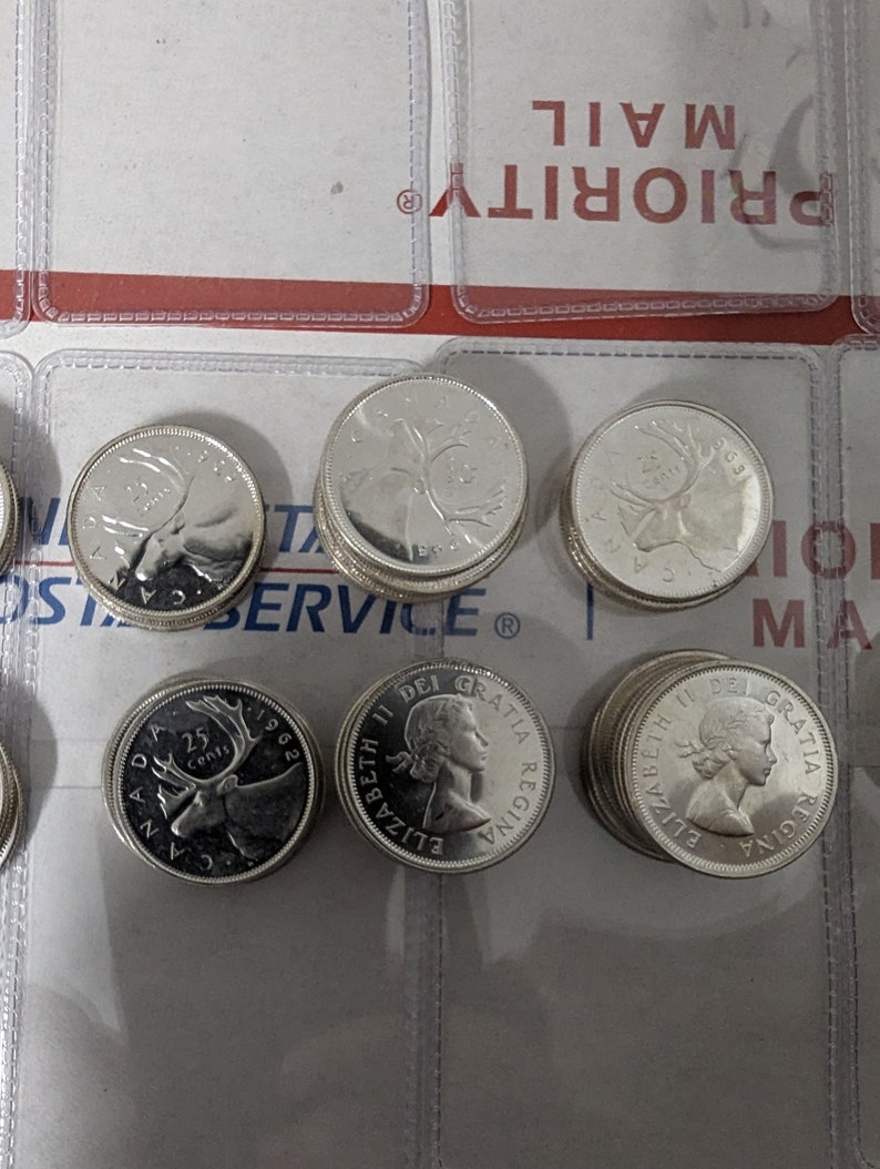 May include: A stack of Canadian 25-cent coins featuring a caribou on one side and a portrait of Queen Elizabeth II on the other. The coins are silver in color and have a smooth, shiny finish.
