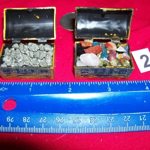 May include: Two small gold treasure chests, one filled with pyrite and the other with a variety of colorful gemstones. The chests are about 1 inch wide and are sitting on a blue ruler.