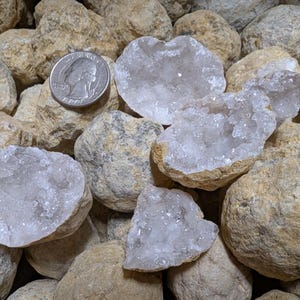 May include: A collection of geode crystals with white quartz crystals inside. The geodes are various sizes and shapes, and some are broken open to reveal the crystals inside.