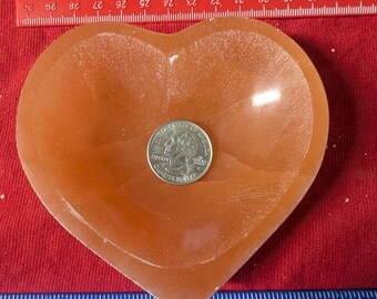 May include: A heart-shaped dish made of orange alabaster. The dish is approximately 4 inches wide and 3 inches tall. A US quarter is placed in the dish for size reference.