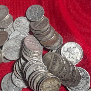 May include: A collection of silver Mercury dimes, displaying the profile of Lady Liberty on the obverse. The coins are scattered on a red surface, showcasing their detailed designs and historical significance. The image highlights the coins' age and wear.