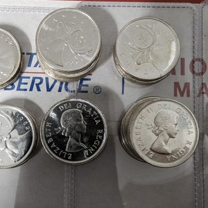 May include: A collection of silver Canadian coins featuring the profile of Queen Elizabeth II and a caribou on the reverse side. The coins are arranged in stacks and are in excellent condition.