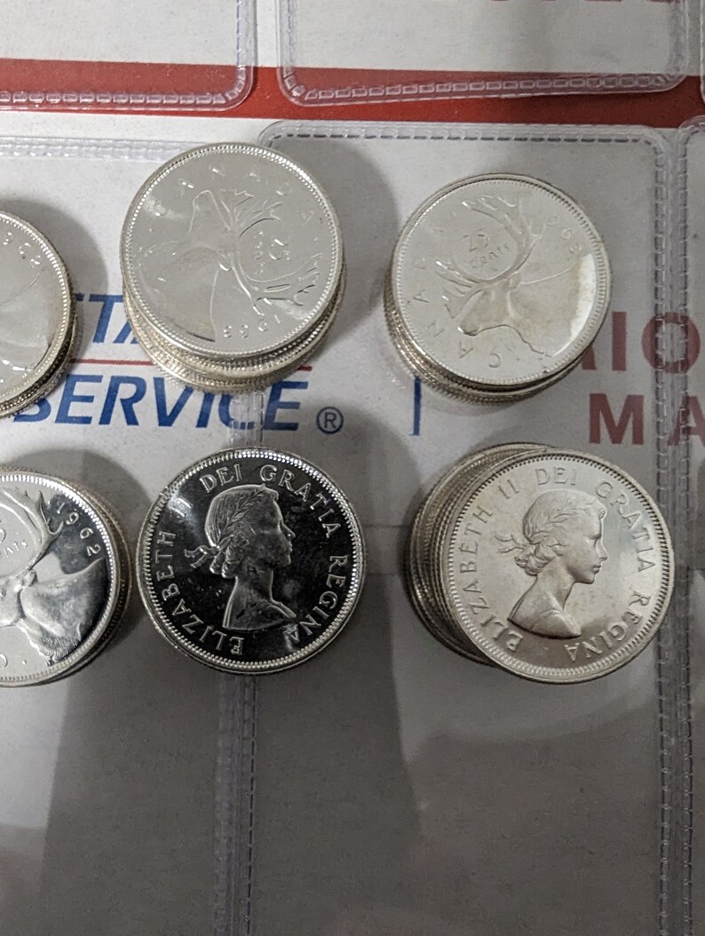 May include: A collection of silver Canadian coins featuring the profile of Queen Elizabeth II and a caribou on the reverse side. The coins are arranged in stacks and are in excellent condition.