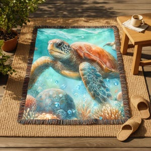 May include: A woven throw blanket with a detailed illustration of a sea turtle underwater. The blanket has a fringed edge and depicts coral, bubbles, and other sea turtles in shades of blue, orange, and green.