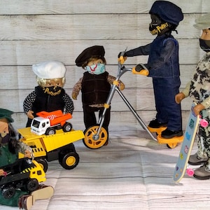 May include: Five dolls wearing face masks and hats, playing with toy vehicles. One doll is riding a scooter, another is on a skateboard, and the other three are playing with toy trucks.