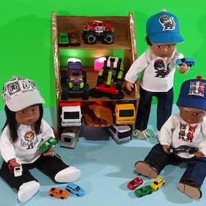 May include: Three dolls wearing hats and shirts with cartoon animal designs are playing with toy cars. The dolls are sitting on a blue surface in front of a wooden shelf with toy cars and trucks.