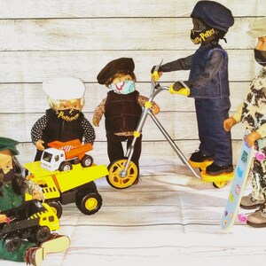 May include: Four dolls wearing face masks and hats, with one doll sitting in green overalls holding a black toy truck, another doll standing by a yellow dump truck, a third doll on a yellow scooter, and a fourth doll holding a skateboard.