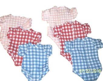 Può includere: Una collezione di cinque body a maniche corte con motivo a quadretti vichy nei toni del rosa chiaro, rosso e blu. I capi sono disposti in gruppo, ognuno con scollo rotondo e chiusura con bottoni a pressione nella parte inferiore.