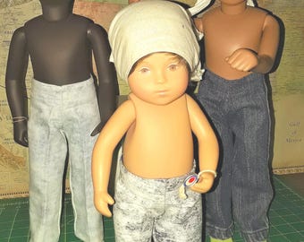 Può includere: Tre bambole in piedi insieme. La bambola a sinistra ha la pelle scura, capelli neri ricci e pantaloni grigio chiaro. La bambola centrale ha la pelle chiara, capelli castani con un foulard beige e pantaloni grigio screziato. La bambola a destra ha la pelle abbronzata, un foulard bianco e jeans blu scuro.