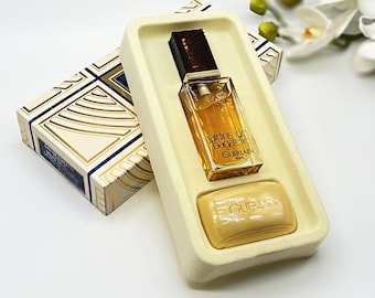 May include: A white box with a gold and blue design contains a small bottle of perfume and a bar of soap. The perfume bottle is labeled "Jardins de Bagatelle Guerlain Paris". The soap is labeled "Guerlain".