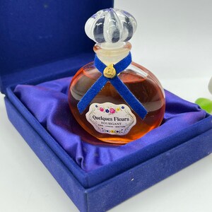 Puede incluir: Un pequeño frasco de perfume Quelques Fleurs Houbigant en una caja de terciopelo azul. El frasco es de vidrio transparente con una cinta azul y un tapón blanco y azul. La etiqueta dice "Quelques Fleurs Houbigant París - Londres - Nueva York".